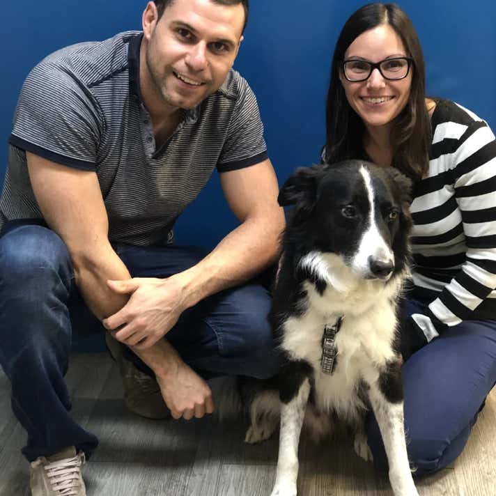 Chico y chica con un perro border collie negro y blanco agachados en la clínica veterinaria El Jardín.