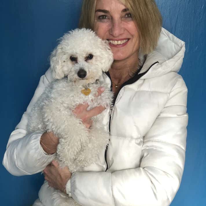 Mujer con un perro caniche blanco en brazos en la clínica veterinaria El Jardín.